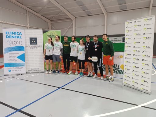 Grupo de personas posando en un evento deportivo con medallas y banners de patrocinadores.r